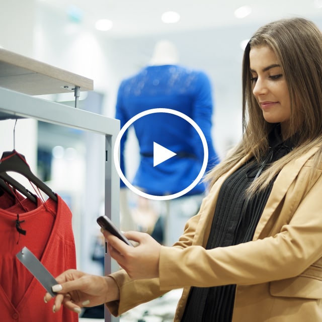 Image of a female customer scanning a price tag of a red blouse with her phone.